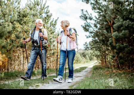 Gerne älteres Paar wandern mit Trekking Stöcke und Rucksäcke an der Junge Kiefernwald. Die Natur genießen, eine gute Zeit auf ihren Ruhestand Stockfoto