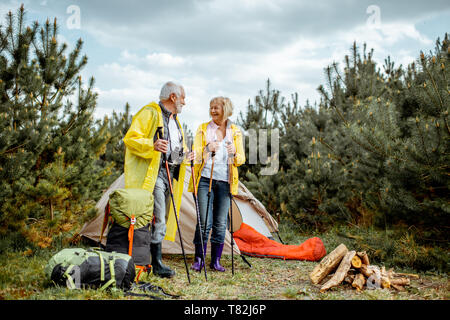 Senior Paar in gelben Regenjacken auf dem Campingplatz mit Zelt und Kamin in der junge kiefernwald Stockfoto