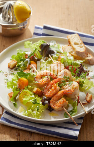 Gegrillten würzigen Scampi oder Baby Hummerschwänze mit Scampi auf Holzspieße auf einem Bett von grünen Salat serviert mit knusprig gebratenen Croutons und in Scheiben geschnitten Stockfoto