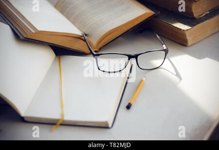 Produkte für die wissenschaftliche Forschung erforderlich: alte Enzyklopädien, ein Notebook mit einem gelben Lesezeichen, Gläser, einen gelben Bleistift und ein offenes Buch mit informieren. Stockfoto