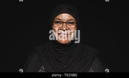 Nahaufnahme von einem lächelnden muslimischen Frau im hijab auf schwarzem Hintergrund isoliert. Arabische Frau in Brillen bei Kamera schaut. Stockfoto