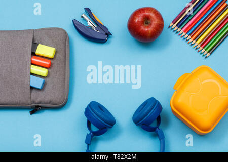 Lunch Box, Buntstifte, Apple, Kopfhörer, Apple, Hefter und Tasche - Federmäppchen mit Farbe filzstifte und Marker auf blauem Hintergrund. Ansicht von oben mit der Kopie Stockfoto