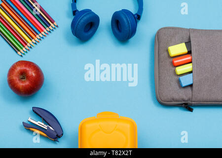 Lunch Box, Buntstifte, Apple, Kopfhörer, Apple, Hefter und Tasche - Federmäppchen mit Farbe filzstifte und Marker auf blauem Hintergrund. Ansicht von oben mit der Kopie Stockfoto