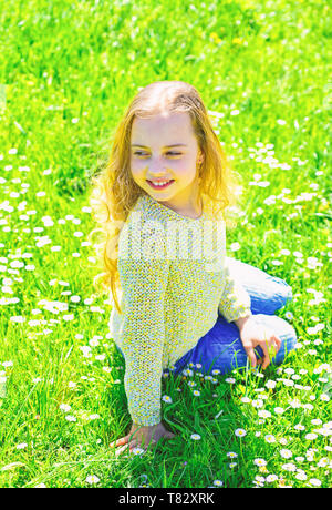 Mädchen sitzt auf Gras an grassplot, grünen Hintergrund. Blütezeit Konzept. Mädchen auf lächelnde Gesicht verbringen Freizeitaktivitäten im Freien. Kind genießen Sie Frühling sonniges Wetter beim Sitzen an der Wiese. Stockfoto