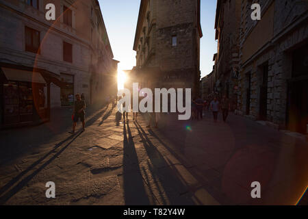 Veautiful Schoß von Menschen zu Fuß durch die alten Straßen von Siena in der Toskana mit der Sonne im Hintergrund, wodurch lange Schatten auf dem Boden Stockfoto