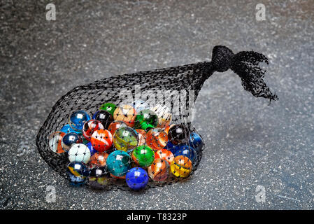 Beutel mit buntem Marmor auf strukturierte Marmortisch, Detailansicht Stockfoto
