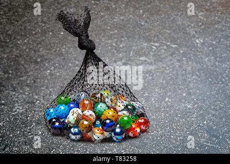 Beutel mit buntem Marmor auf strukturierte Marmortisch, Detailansicht Stockfoto
