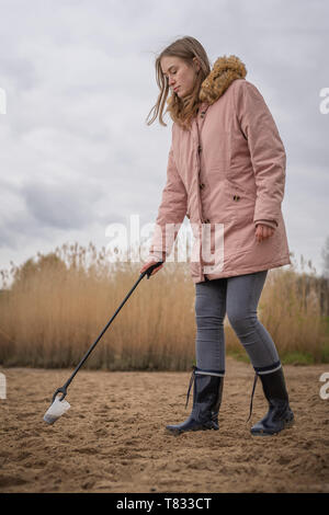 Frau in Gummistiefel sammelt Plastikmüll am Strand mit einer Zange Stockfoto