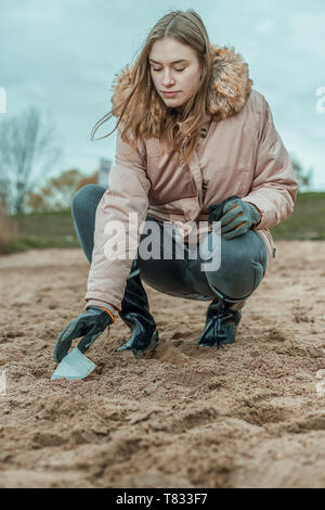 Junge Frau in Stiefeln ist die Reinigung, die den Strand von Kunststoffabfällen von Hand Stockfoto