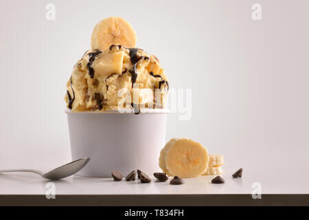 Zusammensetzung der Banane Eis Ball in Pappbecher auf weißen Tisch mit Produkten von Ornament und Ausarbeitung isoliert Hintergrund. Horizontale Zusammensetzung Stockfoto