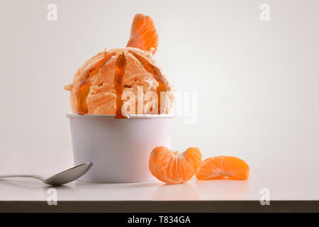 Zusammensetzung von Tangerine Eis Ball in Pappbecher auf weißen Tisch mit Produkten von Ornament und Ausarbeitung isoliert Hintergrund. Horizontale Composit Stockfoto