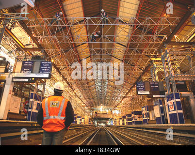 Station Earls Court, London, UK. Ein gerüstbauer Uhren Kollegen installieren Balken über den Titel während einer Nacht-Besitz. Stockfoto