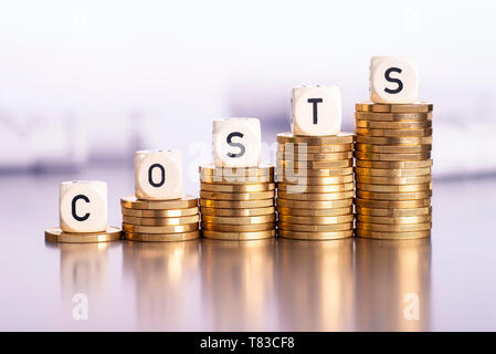 Steigende Stapel von Münzen mit dem Wort Kosten Stockfoto