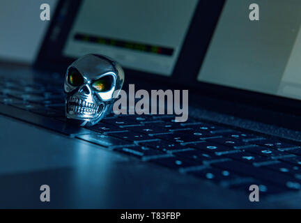Ein Schädel aus glänzendem Metall liegt auf einer Tastatur eines Computers in dunkle Atmosphäre. Stockfoto