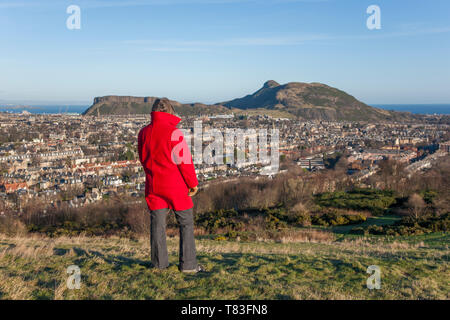 Edinburgh, Edinburgh, Schottland. Frau im roten Mantel bewundern Sie die Aussicht von Blackford Hill über die Dächer zu Arthur's Seat. Stockfoto