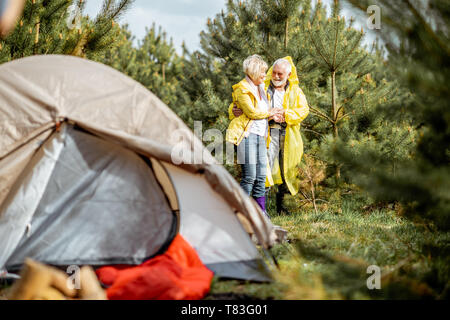 Senior Paar in gelben Regenjacken auf dem Campingplatz im Jungen Wald Stockfoto