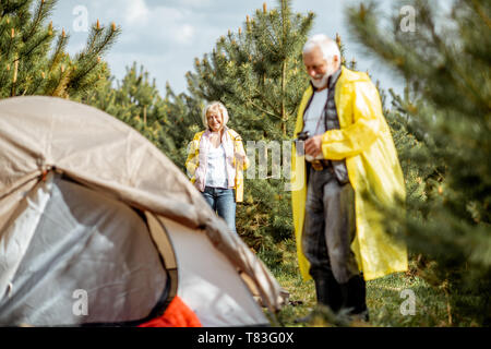 Senior Paar in gelben Regenjacken auf dem Campingplatz im Jungen Wald Stockfoto