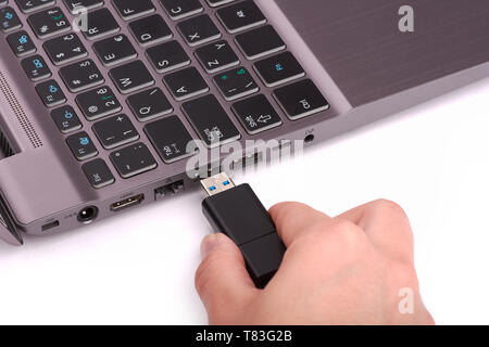 Die Hand einer jungen Frau die Verbindung mit einem USB-Flash-Laufwerk zu einem Hafen in einem silbernen Laptop mit einem schwarzen Tastatur. Auf weissem Hintergrund. Stockfoto