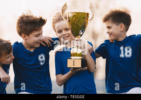 Boys sports Team feiert den Sieg. Glückliche Kinder und goldene Trophäe. Kinder Fußball Team Anhebung der Pokalsieger. Jugend Sport Erfolg Stockfoto