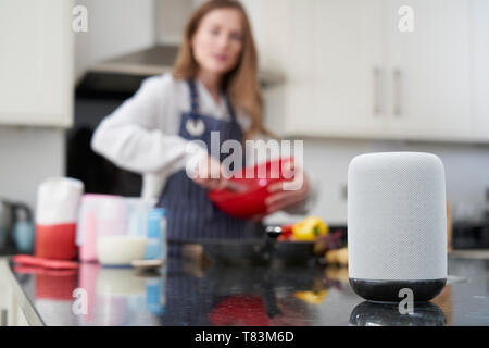 Frau bereitet Speisen zu Hause Fragen Digital Assistant Frage Stockfoto