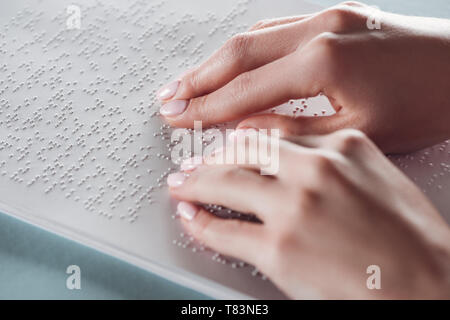 7/8-Ansicht von Mädchen lesen Blindenschrift mit Händen auf weißem Papier Stockfoto