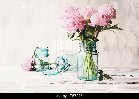 Schöne rosa Pfingstrose Blüten in einer antiken blue Mason jar über einem weißen rustikalen Holztisch Hintergrund mit Kopie Platz für Ihren Text. Stockfoto