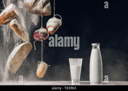 Mehl mit hausgemachtem Brot hängen an Seilen in der Nähe von Spritzer Milch auf schwarzen Hintergrund mit Kopie Raum Stockfoto