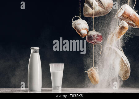 Mehl mit hausgemachtem Brot hängen an Seilen in der Nähe von Spritzer Milch auf Schwarz mit Kopie Raum Stockfoto