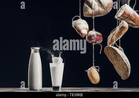 Hausgemachtes Brot hängen an Seilen in der Nähe von Spritzer Milch isoliert auf Schwarz mit Kopie Raum Stockfoto