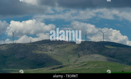 Landschaft mit weißen Wolken und Windenergieanlagen. Windräder entlang der Weise auf dem Hügel. Stockfoto