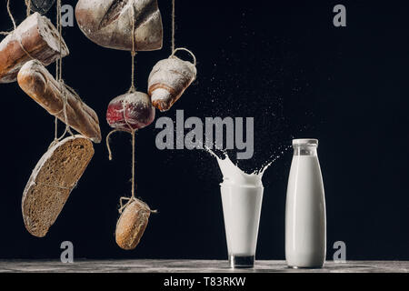 Hausgemachtes Brot hängen an Seilen in der Nähe von Spritzer Milch isoliert auf Schwarz Stockfoto