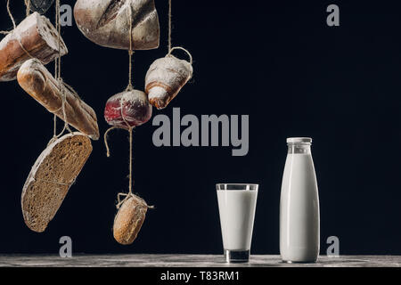 Milch auf dem Tisch und das Brot mit Mehl hängen auf Strings isoliert auf Schwarz mit Kopie Raum Stockfoto