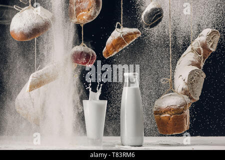 Milch Spritzen in Glas auf den Tisch und vier Fallen auf Brot hängen auf Strings isoliert auf Schwarz Stockfoto