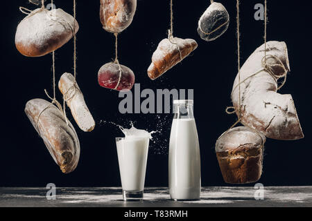 Milch Spritzen in Glas auf dem Tisch und das Brot mit Mehl hängen auf Strings isoliert auf Schwarz Stockfoto