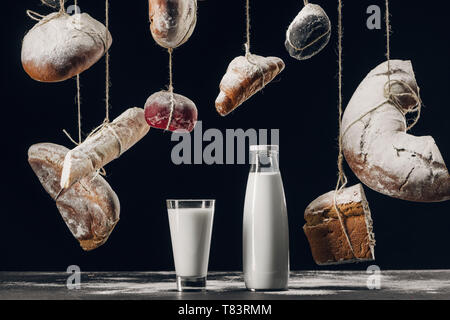 Milch auf dem Tisch und das Brot mit Mehl hängen auf Strings isoliert auf Schwarz Stockfoto