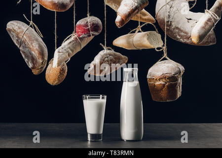 Milch in Glas und Flasche auf dem Tisch und das Brot mit Mehl hängen auf Strings isoliert auf Schwarz Stockfoto