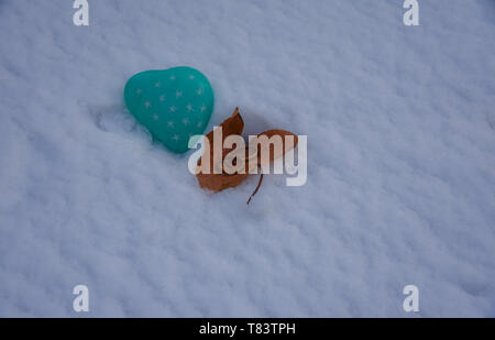 Zwei goldene Hochzeit Ringe in einem Herbstlich gefärbte Blätter, die an einem herzförmigen grünen Stein auf einem frischen Schnee Hintergrund. Kopieren Sie Platz. Stockfoto