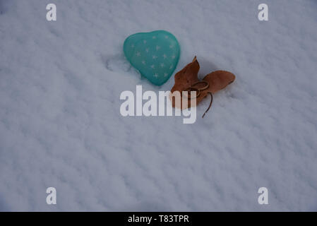 Zwei goldene Hochzeit Ringe in einem Herbstlich gefärbte Blätter, die an einem herzförmigen grünen Stein auf einem frischen Schnee Hintergrund. Kopieren Sie Platz. Stockfoto