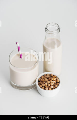 Kichererbsen in der Schüssel in der Nähe von Flasche und Glas mit vegan Kichererbse Milch auf grauem Hintergrund Stockfoto