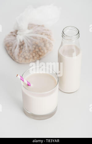 Kichererbse in Gaze in der Nähe von Flasche und Glas mit vegan Kichererbse Milch auf grauem Hintergrund Stockfoto