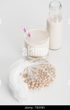 Kichererbsen in Weiß Gaze in der Nähe von Flasche und Glas mit vegan Kichererbse Milch auf grauem Hintergrund Stockfoto