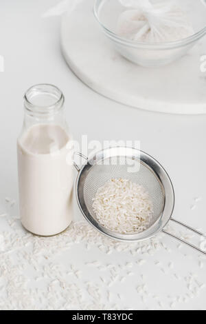 Selektiver Fokus von Reis Milch in der Flasche in der Nähe von Reis und Sieb mit Reis im seihtuch auf Hintergrund Stockfoto