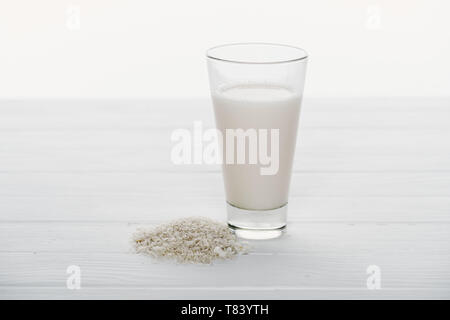 Reis Milch in Glas in der Nähe von Reiskörnern auf Holztisch auf Weiß isoliert Stockfoto