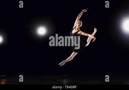 Ballerina in einen schwarzen Anzug ist das Springen auf einem schwarzen Hintergrund. Stockfoto