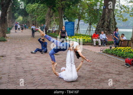 Ein junges Paar Akrobatik auf dem Gehsteig auf der Seite der Hoan Kiem See in der Altstadt von Hanoi, Vietnam, Südostasien Stockfoto