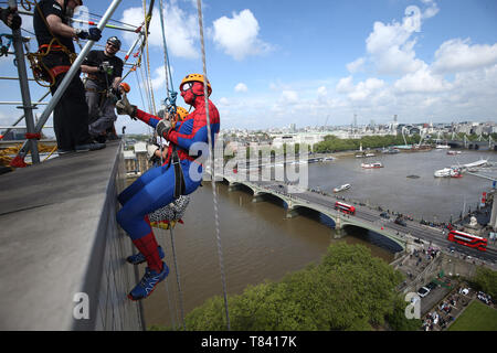 Ein Mann in einem Spider-man-Kostüm gibt den Daumen nach oben, als er sich im Rahmen einer Spendenaktion für das Evelina London Children's Hospital auf der Spitze des St. Thomas' Hospital in London abseilen will. Stockfoto