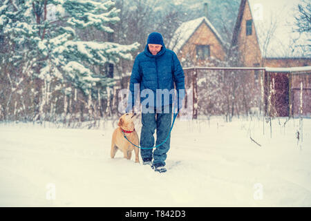 Mensch und Hund sind die besten Freunde. Ein Mann mit einem Hund geht in einem Dorf in einer verschneiten Winter Stockfoto