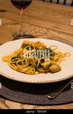 Hausgemachte Spaghetti mit Spinat und Huhn am Tisch mit einem Glas Wein. Traditionelle biologische Lebensmittel. Stockfoto