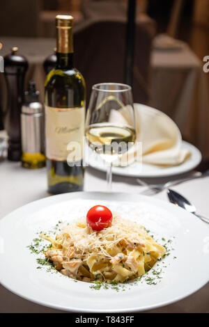 Cremige Nudeln mit Huhn und Käse serviert in tiefen Teller mit weißem Glas Wein. Italienisches Essen Stockfoto