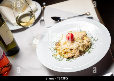 Cremige Nudeln mit Huhn und Käse serviert in tiefen Teller mit weißem Glas Wein. Italienisches Essen Stockfoto